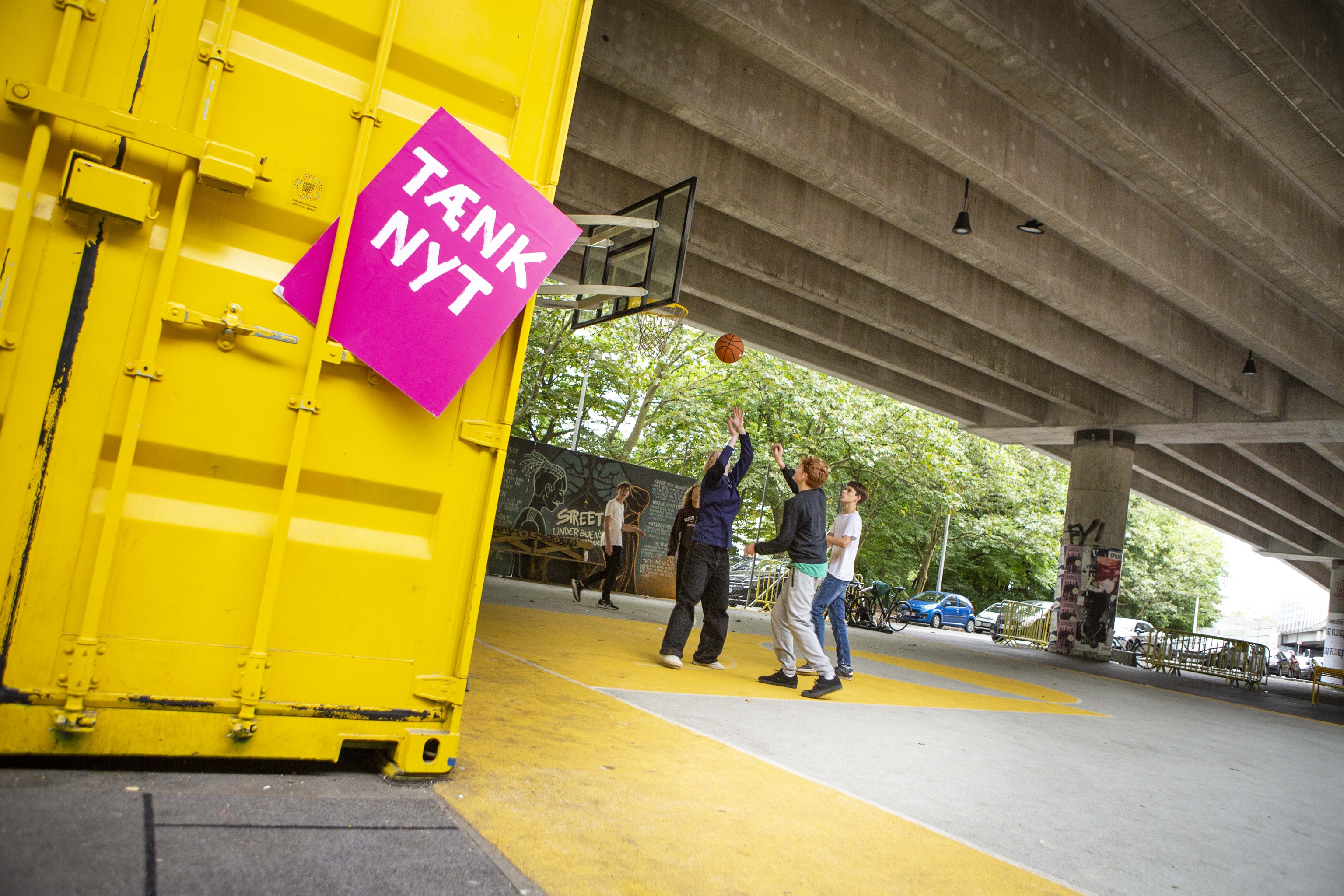 Tænk nyt-skilt ved en gul container, hvor unge mennesker spiller basket